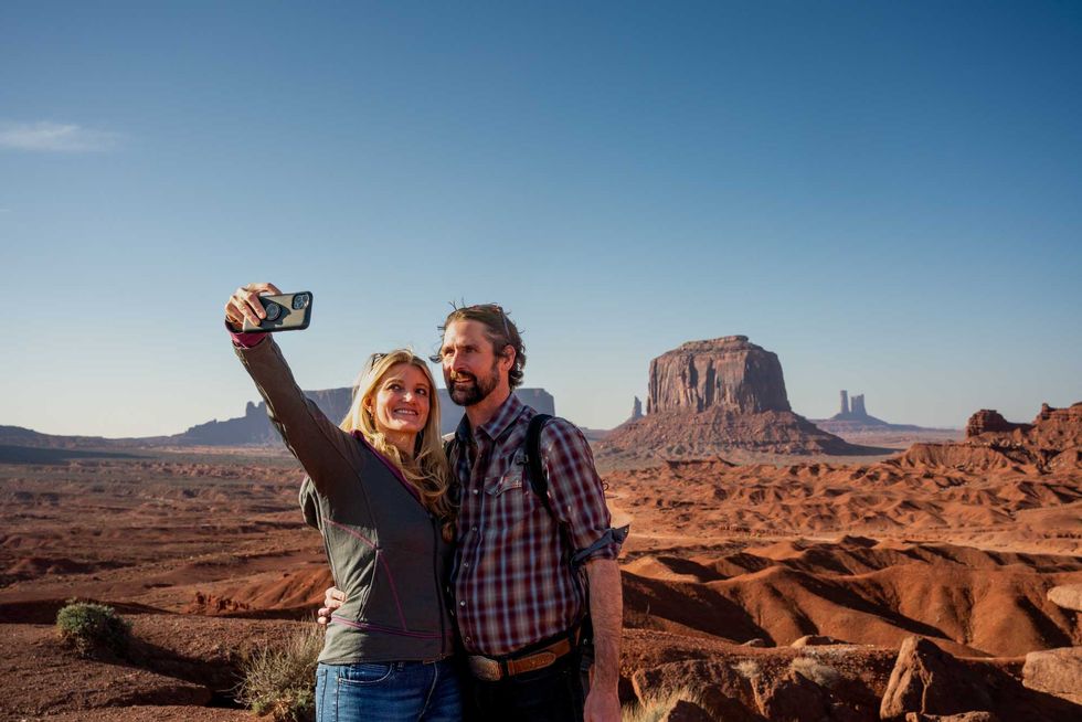 Couple taking selfie in Monument Valley desert landscape under clear blue sky.