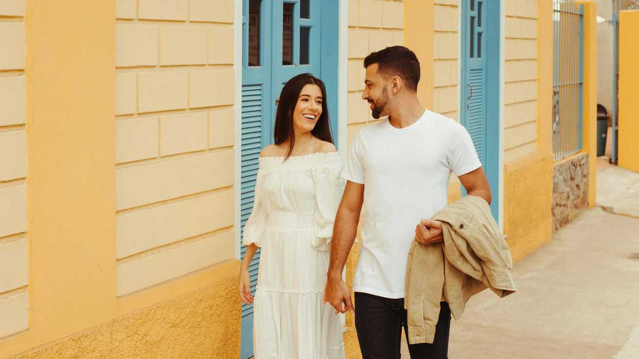 Couple walking hand in hand on a colorful street, smiling at each other.