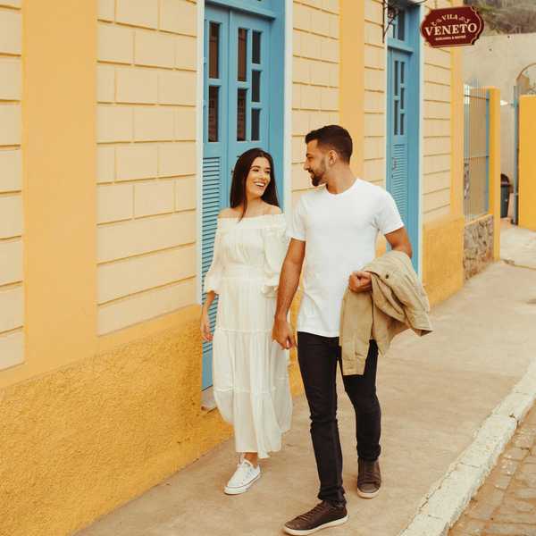 Couple walking hand in hand on a colorful street, smiling at each other.