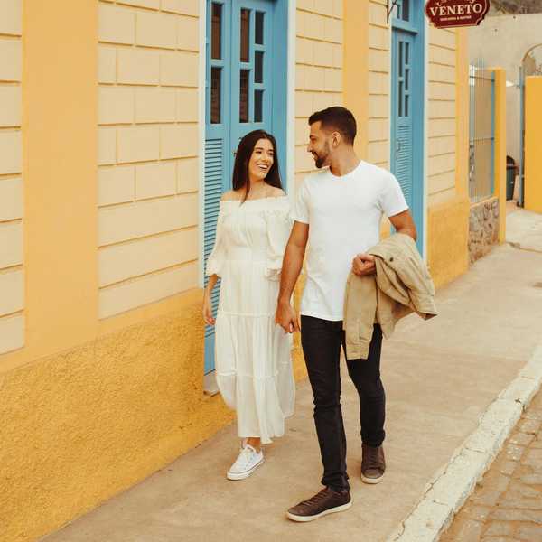 Couple walking hand in hand on a colorful street, smiling at each other.