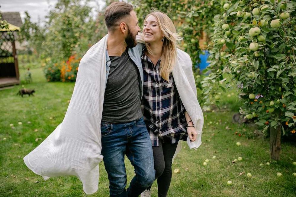 Couple walking in an orchard, wrapped in a blanket and smiling.