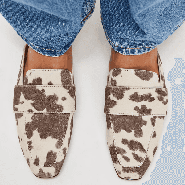 Cow-print loafers and blue jeans from a top-down view.