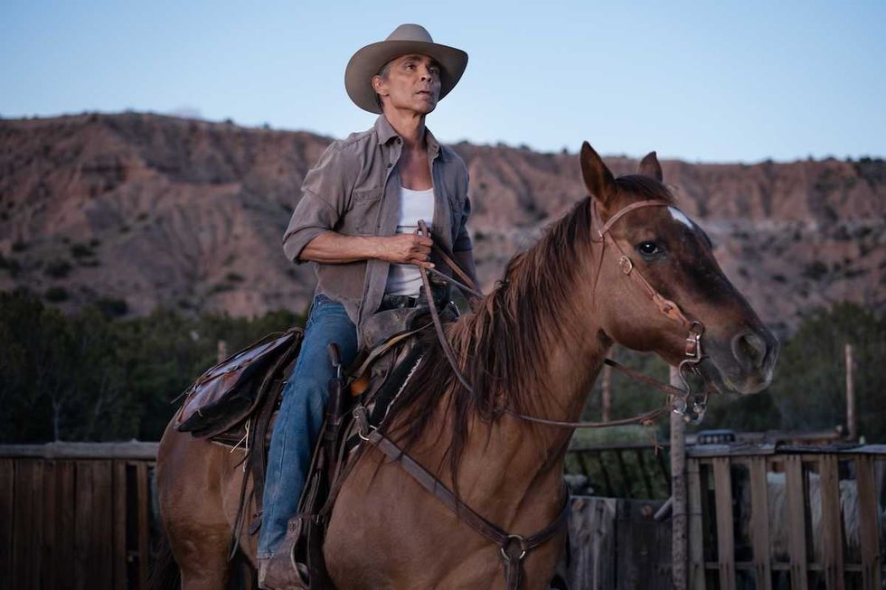 Cowboy on horseback against a rugged mountainous backdrop at dusk.