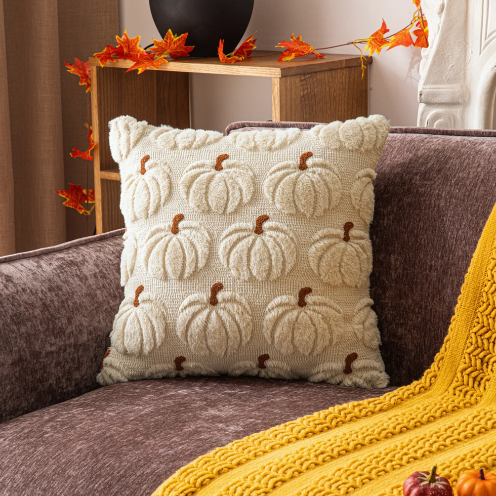 Cozy autumn scene with pumpkin-patterned pillow and yellow knit blanket on a couch.