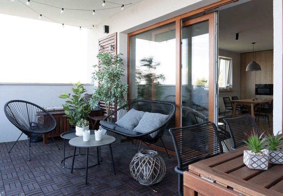Cozy balcony with modern chairs, plants, and string lights; adjoining a wooden-floored room.