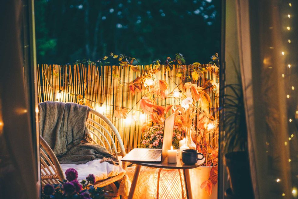 Cozy balcony with string lights, a laptop on a table, and a wicker chair with a blanket.