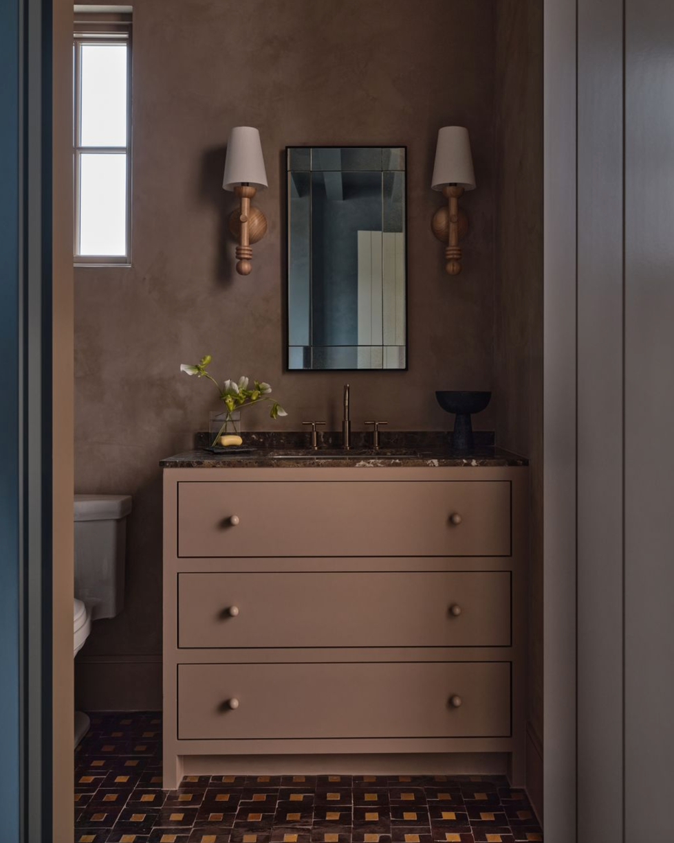 Cozy bathroom with dresser, mirror, wall lamps, and checkered brown floor tiles.