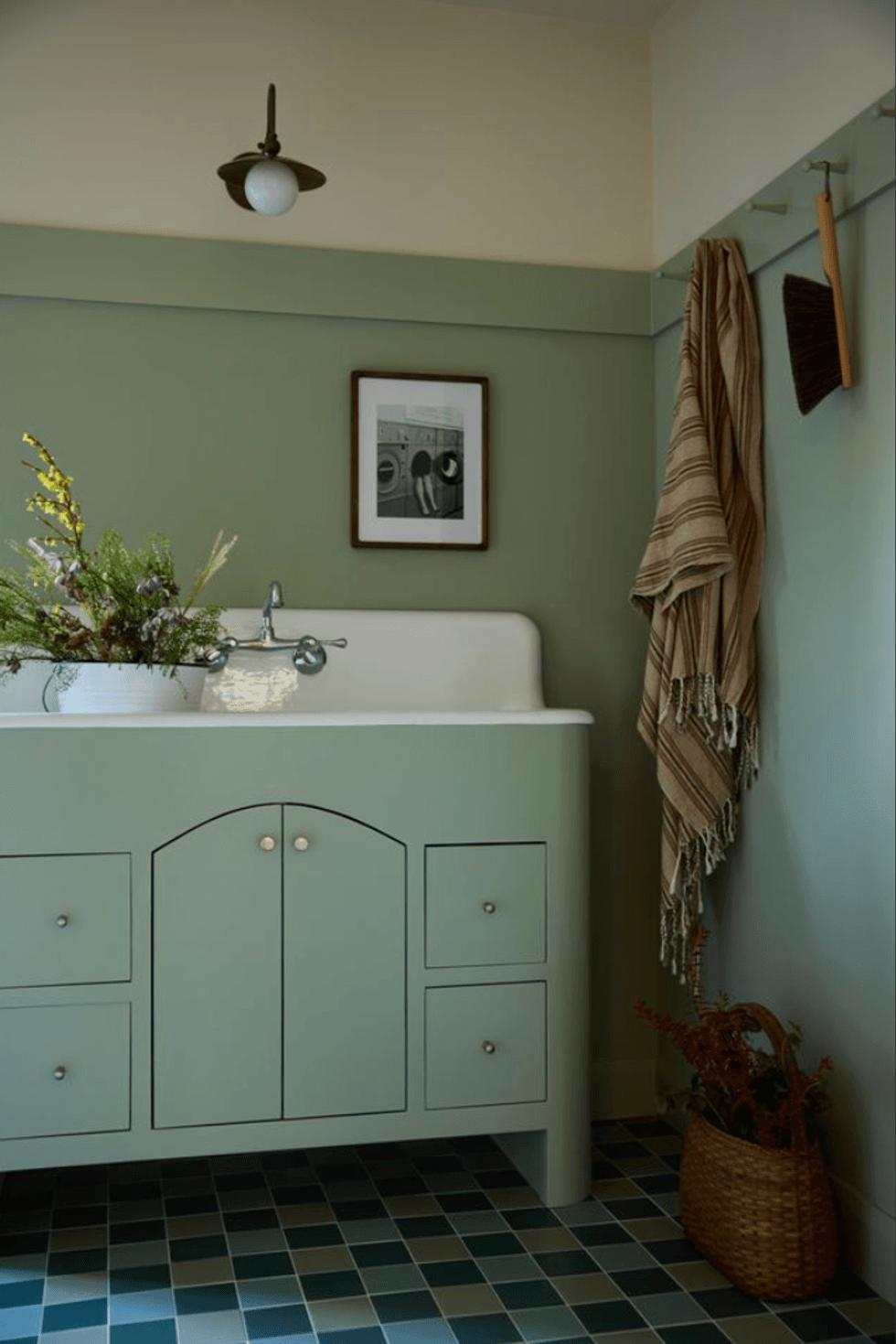 Cozy bathroom with green vanity, striped towel, basket, and framed art.