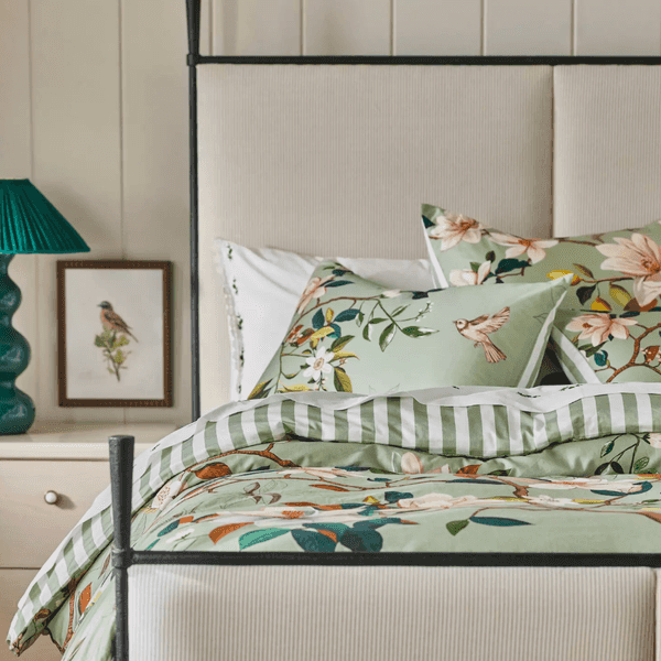 Cozy bed with green floral bedding, striped sheets, and bird-themed decor.