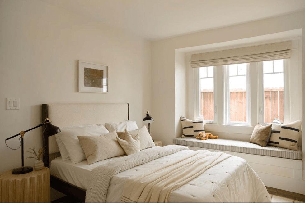 Cozy bedroom with a bed, window seat, soft lighting, and neutral decor.