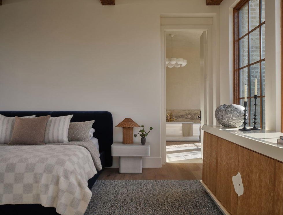 Cozy bedroom with a checkered blanket, pillows, and a view into a bright bathroom.