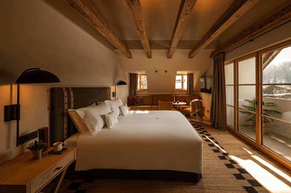 Cozy bedroom with a large bed, wooden beams, and a sunlit balcony.