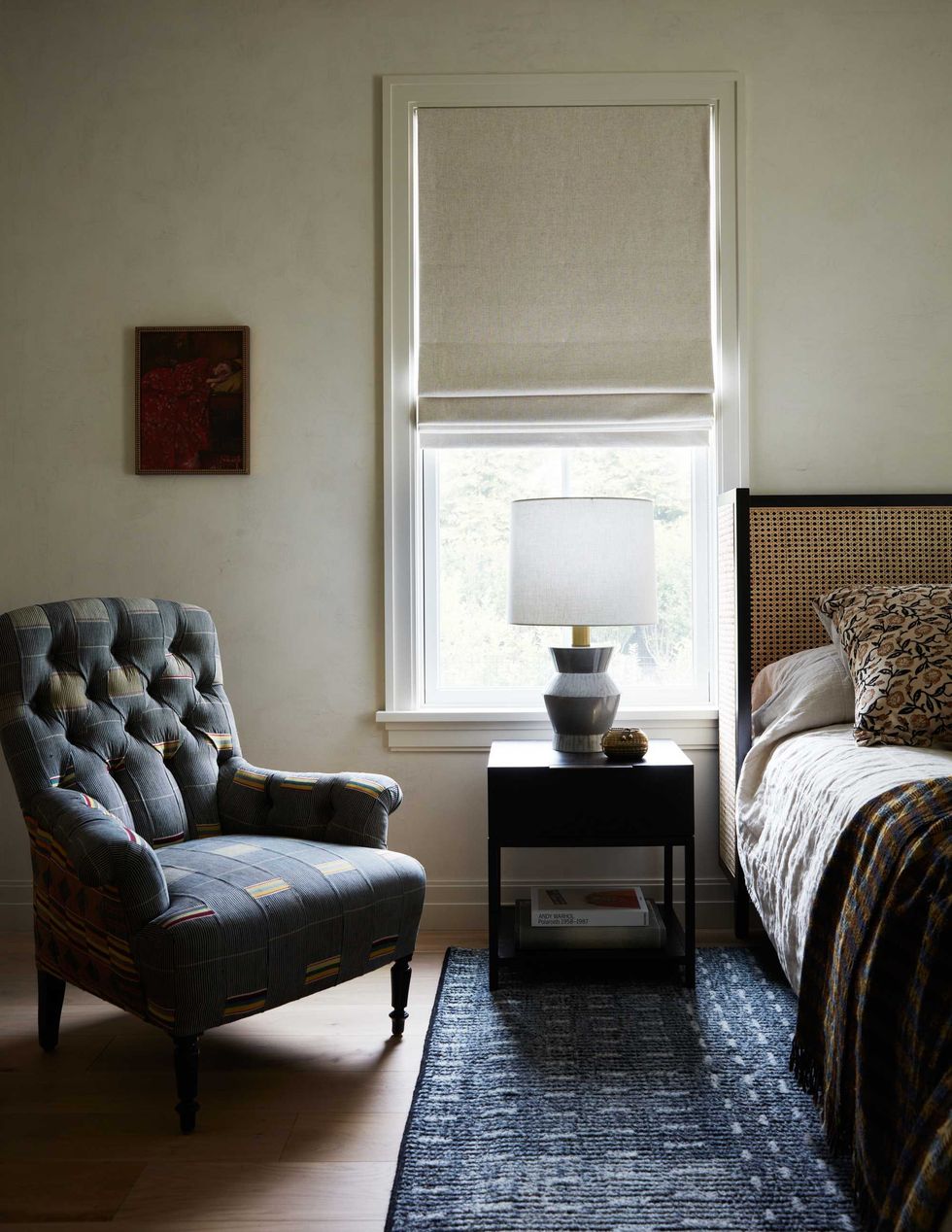 Cozy bedroom with armchair, window, nightstand, and bed with patterned rug and blanket.