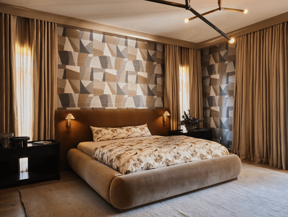 Cozy bedroom with geometric wallpaper, plush bed, warm lighting, and thick curtains.