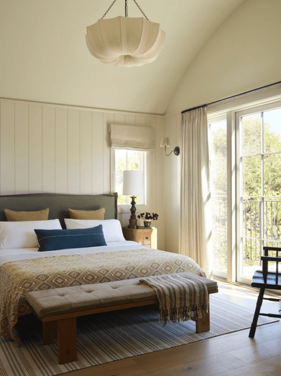 Cozy bedroom with large bed, pendant light, and glass doors leading to a balcony with greenery.