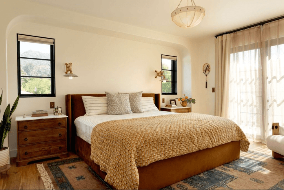 Cozy bedroom with large bed, wooden dressers, and soft natural light through sheer curtains.