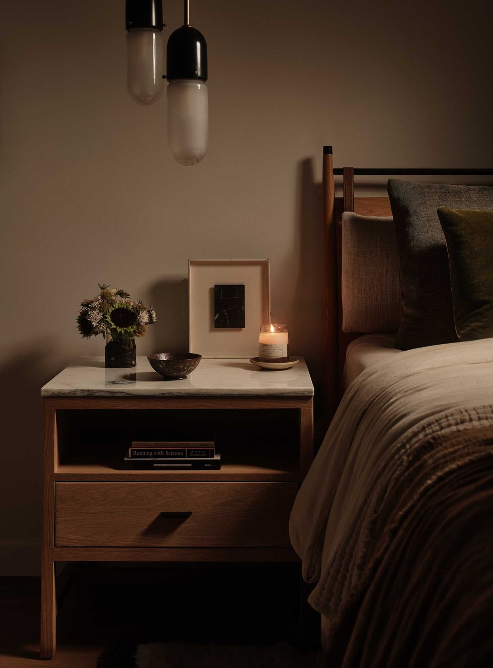 Cozy bedroom with pendant lights and a nightstand holding flowers, a photo, and a lit candle.