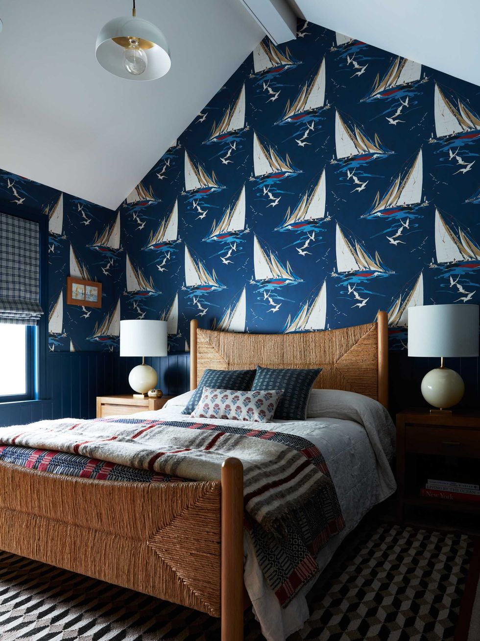 Cozy bedroom with sailboat wallpaper, woven bedframe, and patterned bedding.