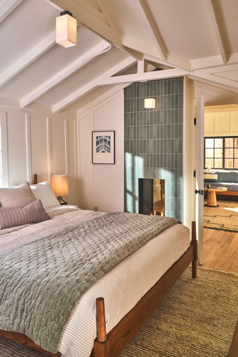 Cozy bedroom with wood bed, soft lighting, and a green tiled fireplace.