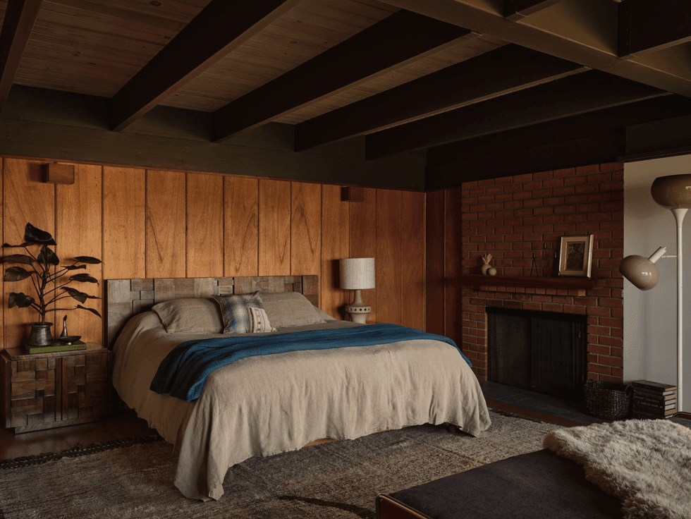 Cozy bedroom with wood paneling, fireplace, and a large bed with beige and blue accents.