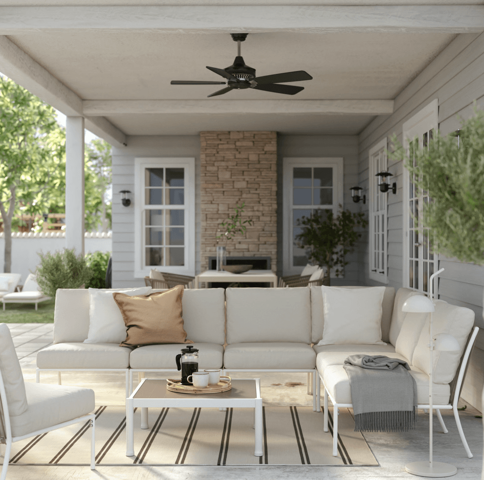 Cozy covered patio with beige couches, striped rug, coffee table, and stone fireplace.