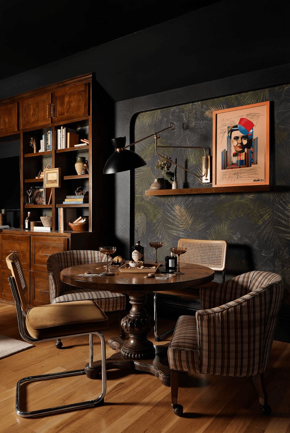 Cozy dining area with vintage table, chairs, art, and bookshelf on wooden floor.