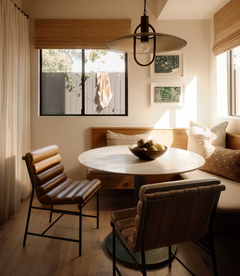 Cozy dining nook with a round table, leather chairs, and sunlight streaming through windows.