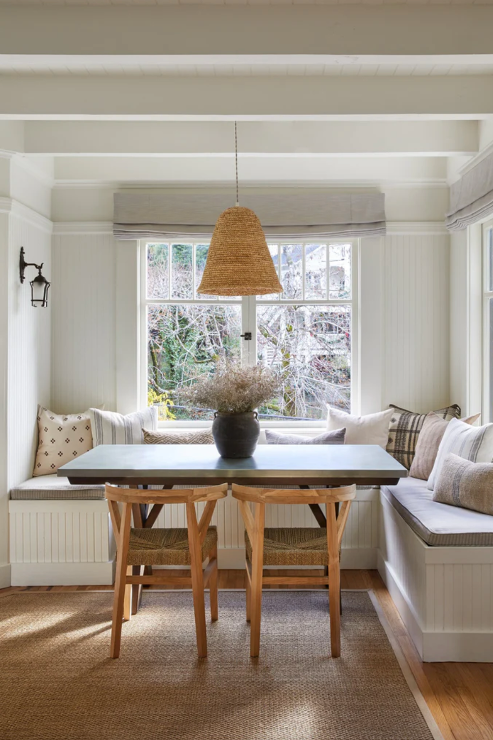 Cozy dining nook with bench seating, wooden table, and pendant light by a large window.