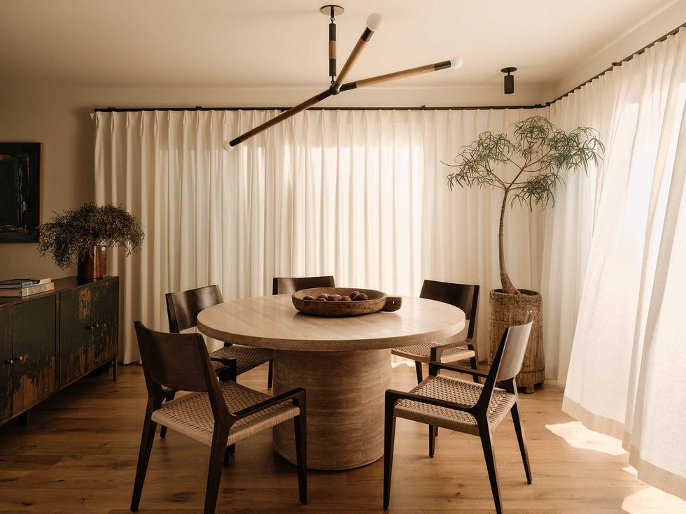 Cozy dining room with round table, five chairs, modern light, and draped curtains.
