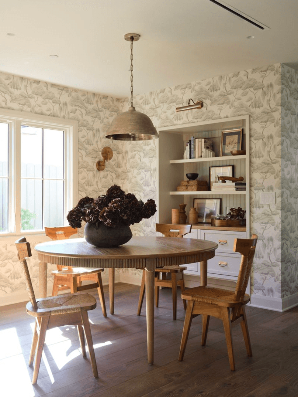 Cozy dining room with round wooden table, chairs, and floral wallpaper.
