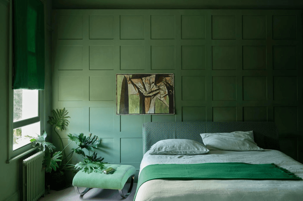 Cozy green bedroom with panel wall, plants, and modern art above the bed.