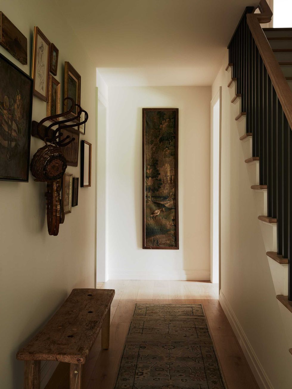 Cozy hallway with framed art, wooden bench, and staircase on the right.