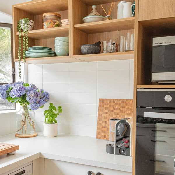 Cozy kitchen corner with flowers, basil, and espresso machine on white countertop.