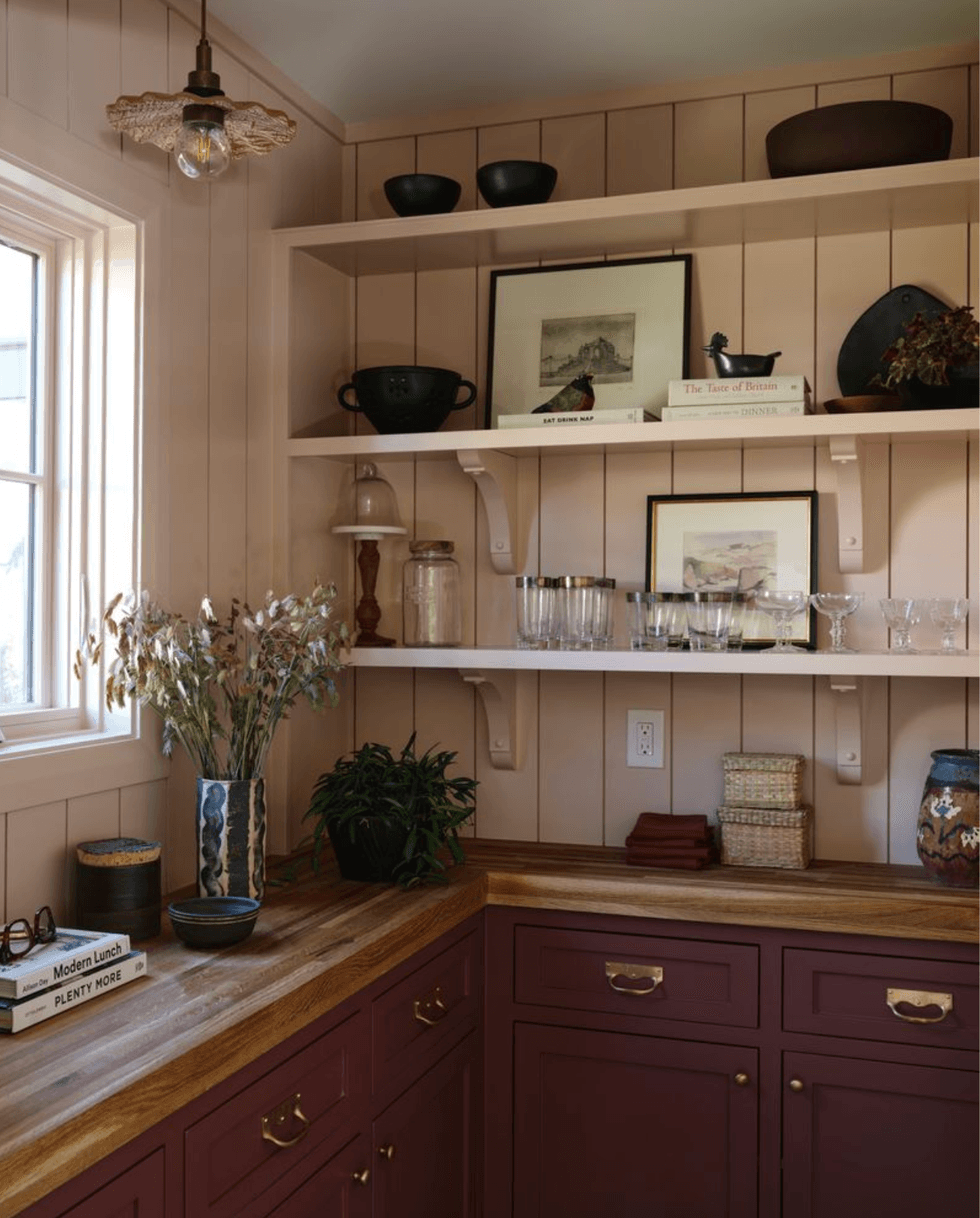 Cozy kitchen corner with red cabinets, wooden shelves, books, and decorative kitchenware.