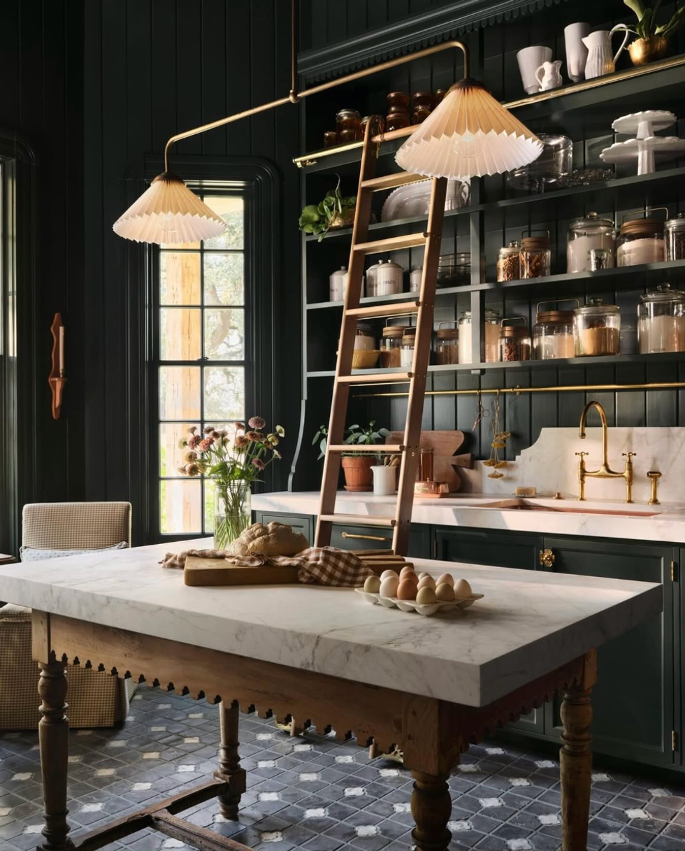 Cozy kitchen with a marble-top table, vintage ladder, and open shelves under warm lighting.