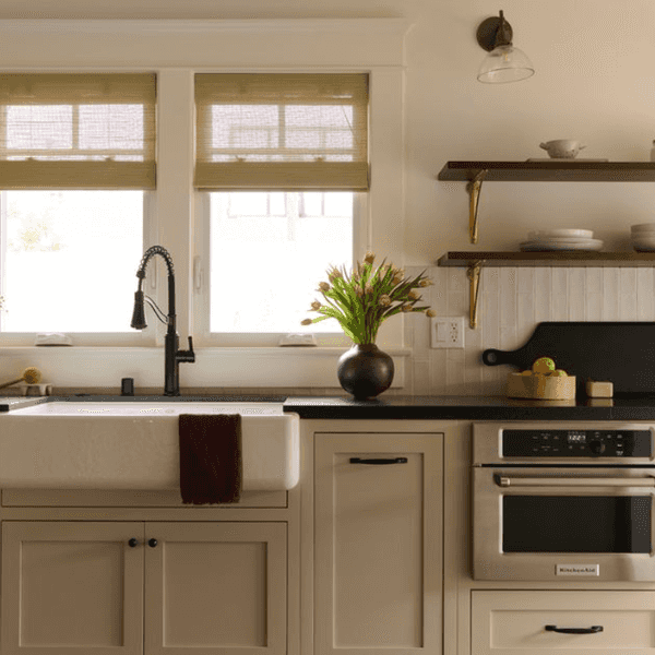 Cozy kitchen with farmhouse sink, vase of flowers, open shelves, and a large window.