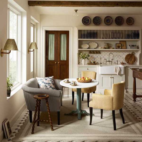 Cozy kitchen with rustic beams, round table, and striped sofa by large windows.