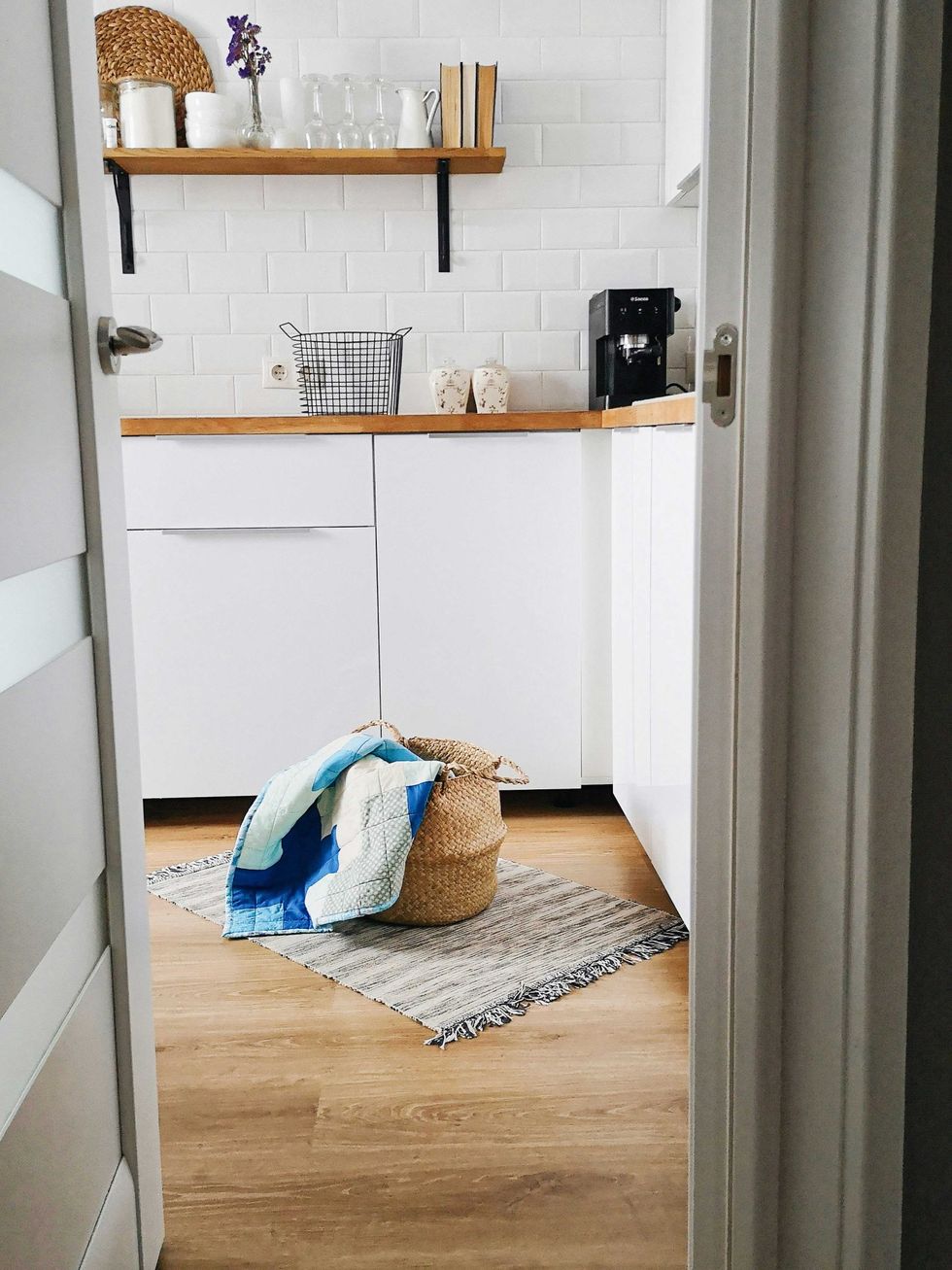 Cozy kitchen with white cabinets, shelf, rug, and a basket holding a colorful quilt.