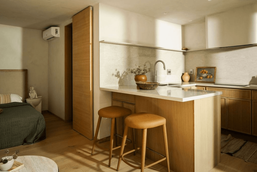 Cozy kitchen with wooden accents, island, and stools next to a small bed area.
