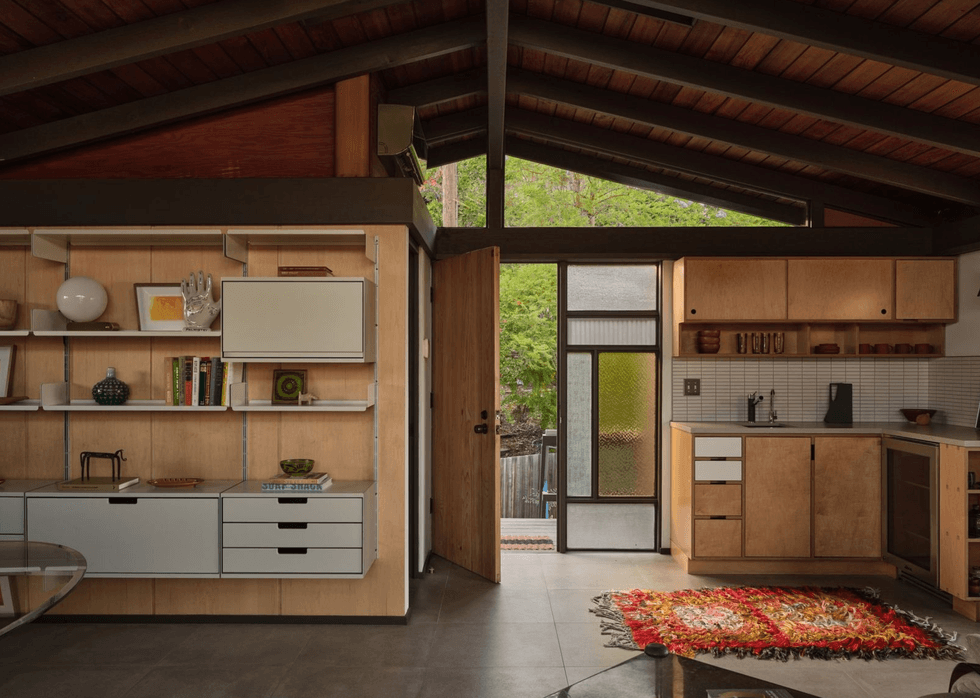 Cozy kitchen with wooden cabinets, open door, colorful rug, and modern shelving.