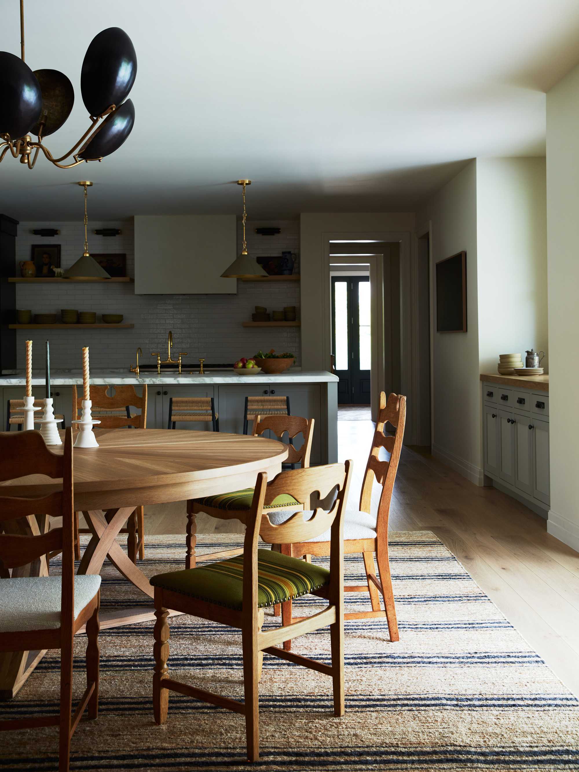 Cozy kitchen with wooden dining set, striped rug, pendant lights, and black chandelier.