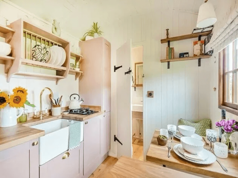 Cozy kitchen with wooden shelves, sunflowers, and a small dining table set by the window.
