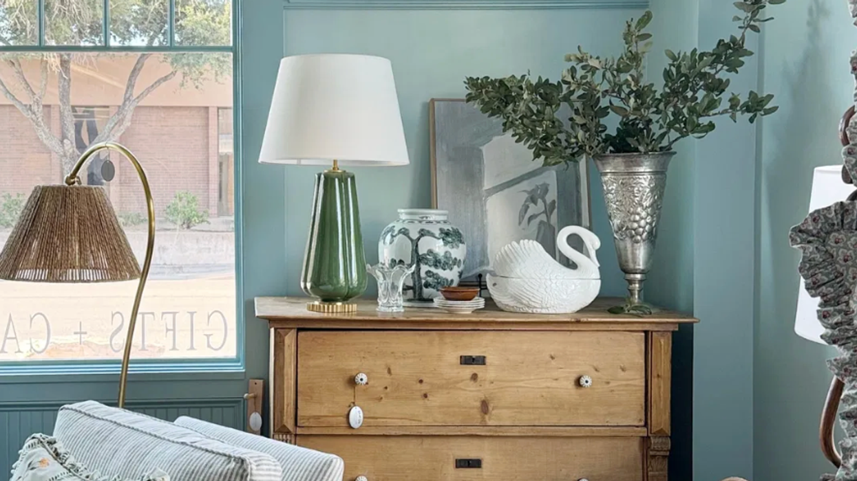 Cozy living room corner with wooden dresser, plants, art, and comfortable seating.