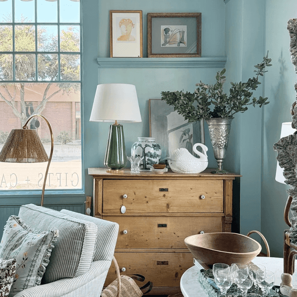 Cozy living room corner with wooden dresser, plants, art, and comfortable seating.