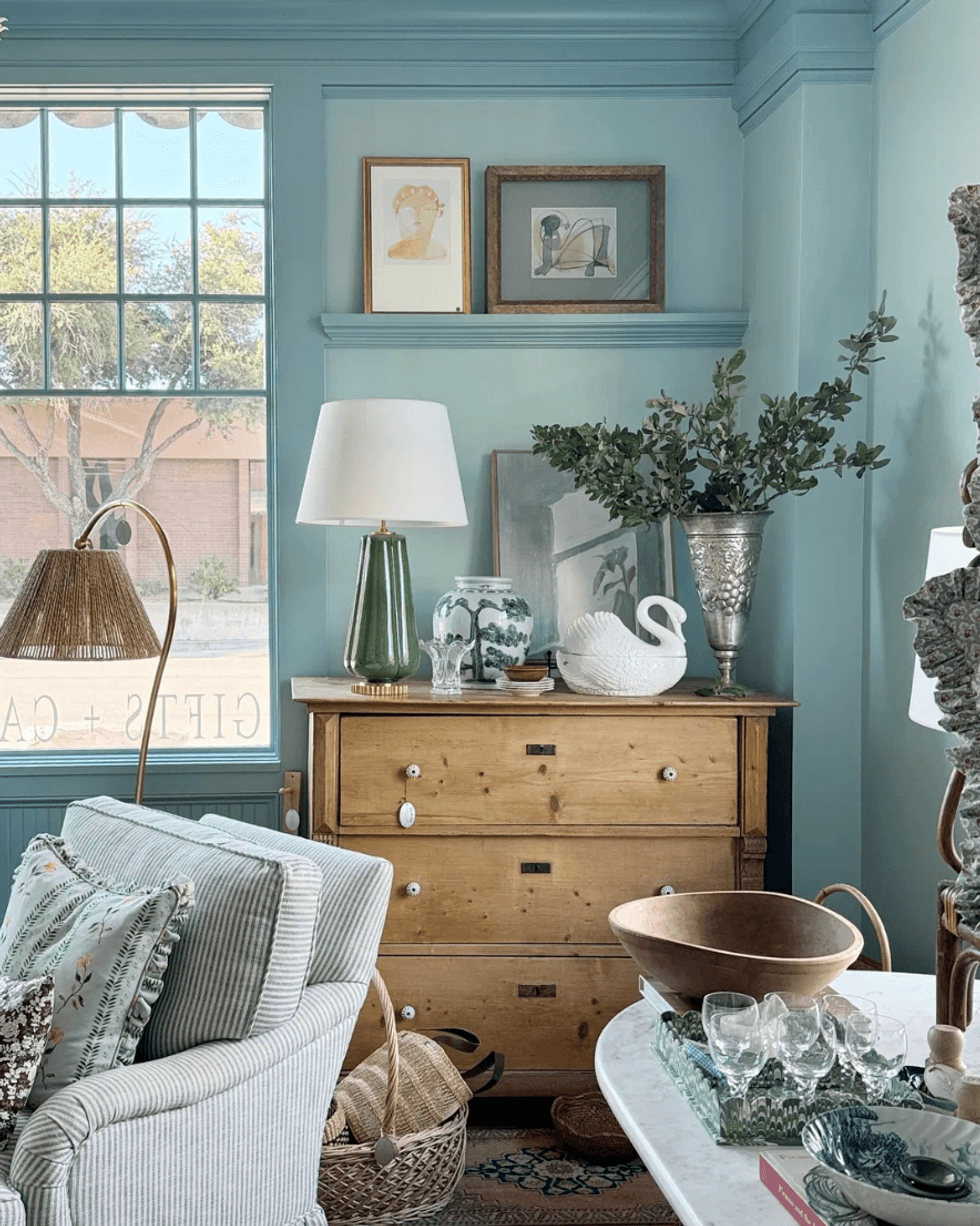 Cozy living room corner with wooden dresser, plants, art, and comfortable seating.