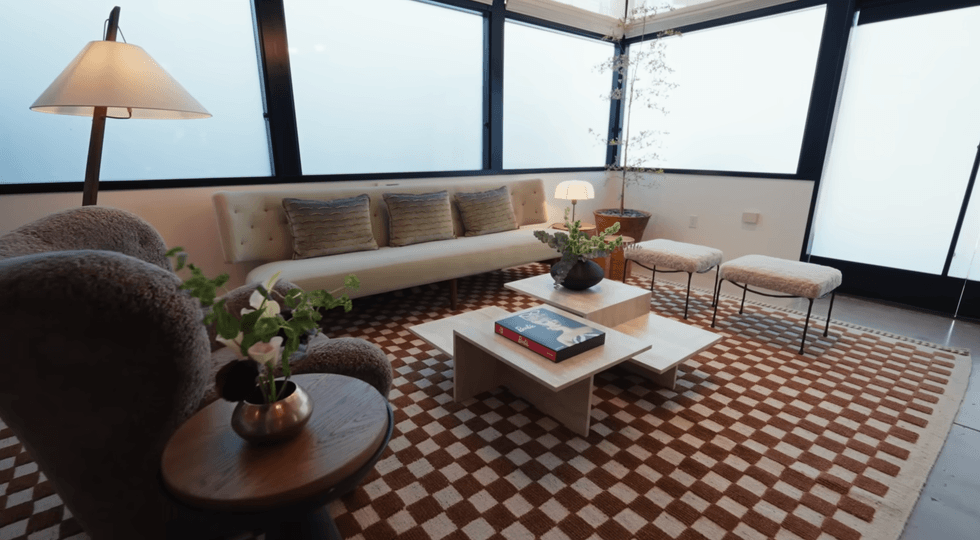 Cozy living room with a sofa, armchair, checkered rug, and large windows.