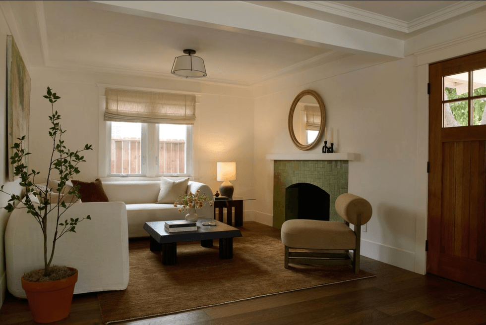 Cozy living room with a sofa, chair, round mirror, and a green-tiled fireplace.