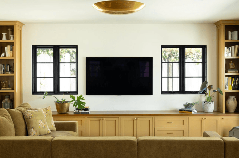 Cozy living room with beige couch, TV, built-in shelves, and two windows.