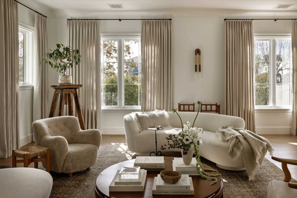 Cozy living room with beige sofas, plants, and large windows letting in natural light.