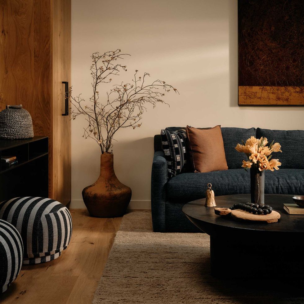 Cozy living room with dark sofa, striped poufs, and rustic decor elements.